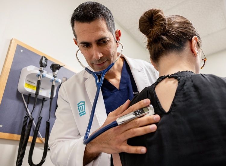 Arzt misst bei einer Patientin mit Stethoskop und Blutdruckmanschette die Vitalzeichen